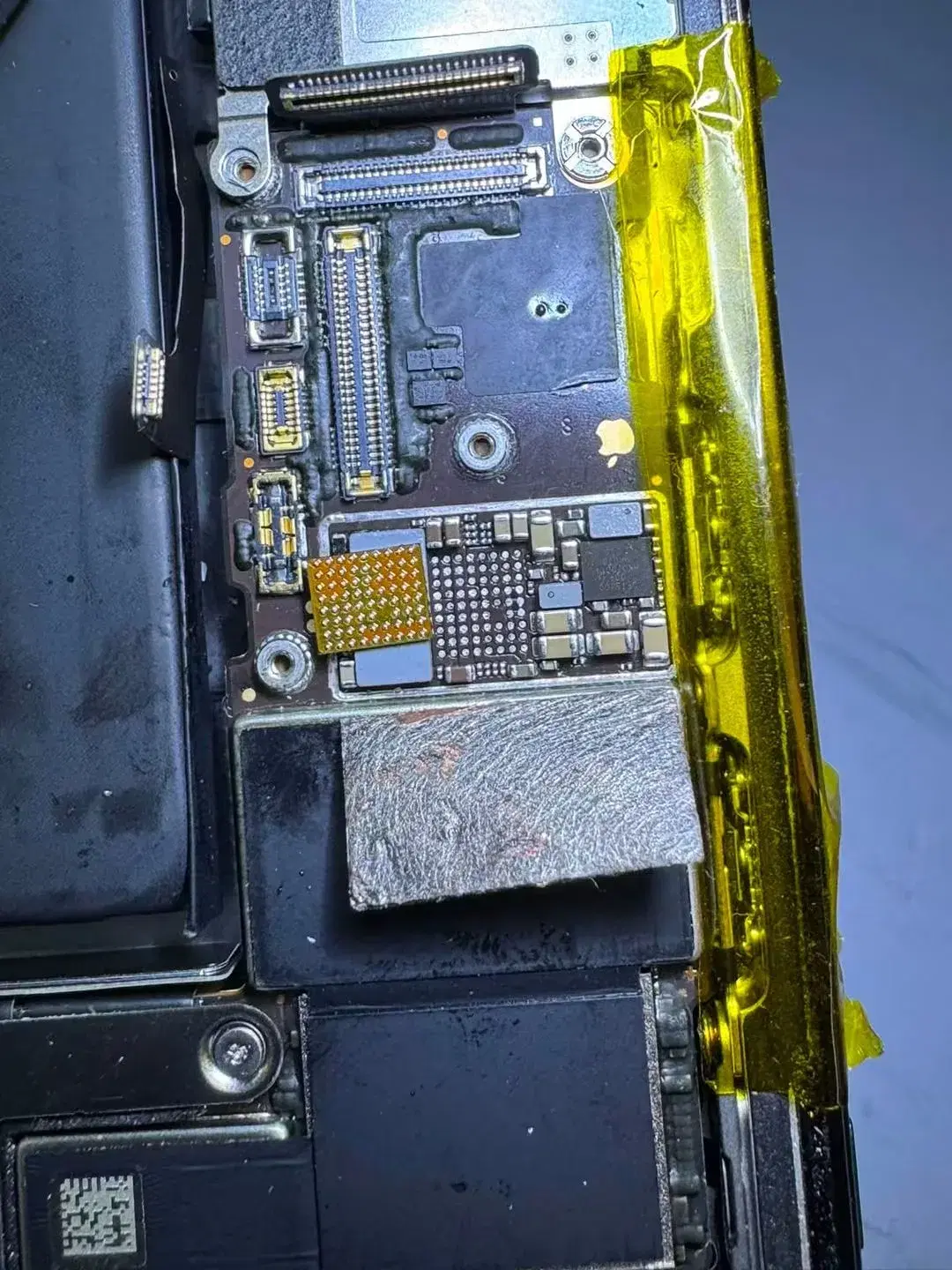 An iPhone logic board inside the phone with the shield lifted and one chip removed, exposing its solder pads