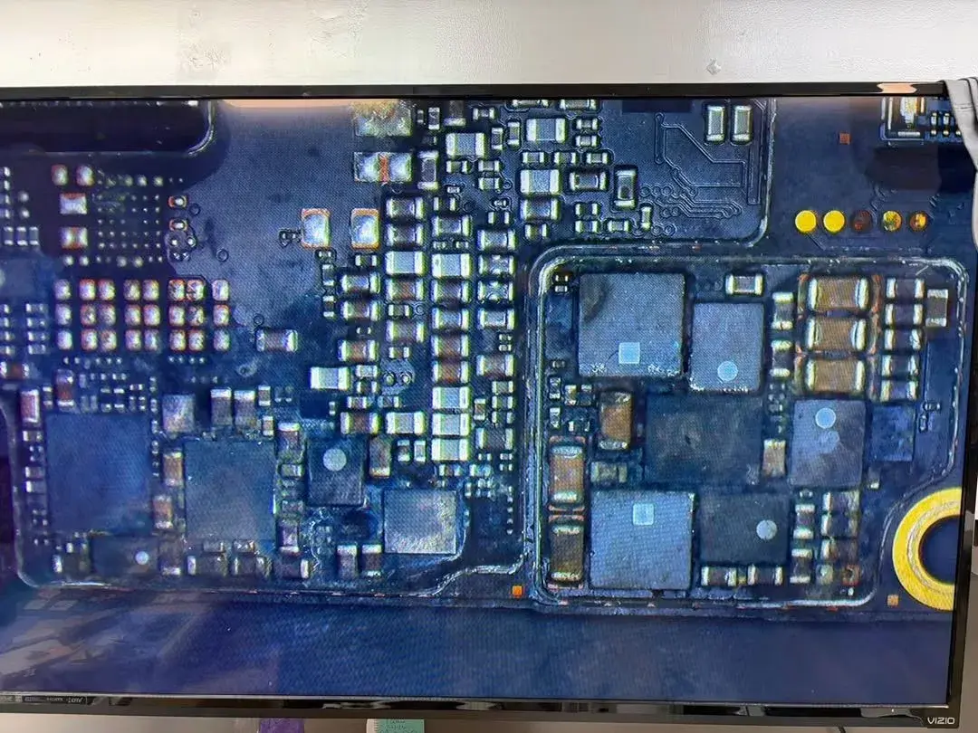 A microscope view of an iPhone logic board on a monitor, showing the small parts checked during board repair