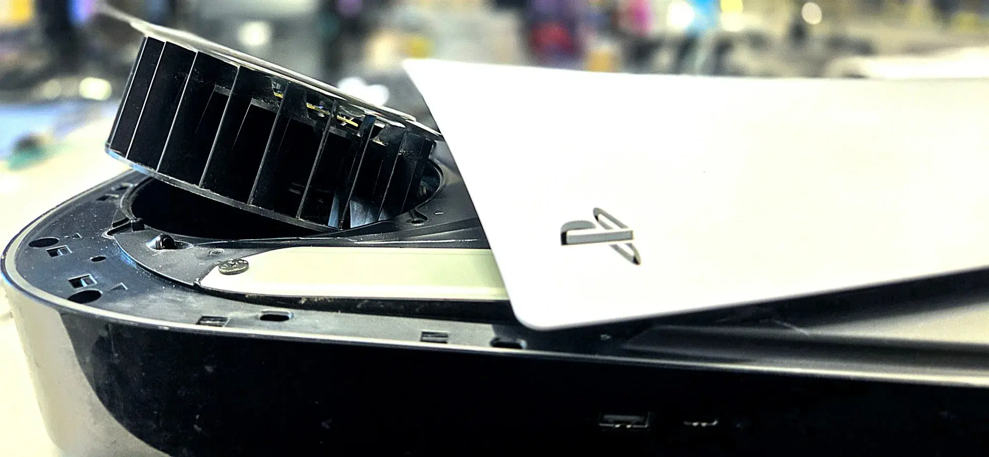 A PS5 with its white side panel lifted and the black blower fan tilted up out of its housing