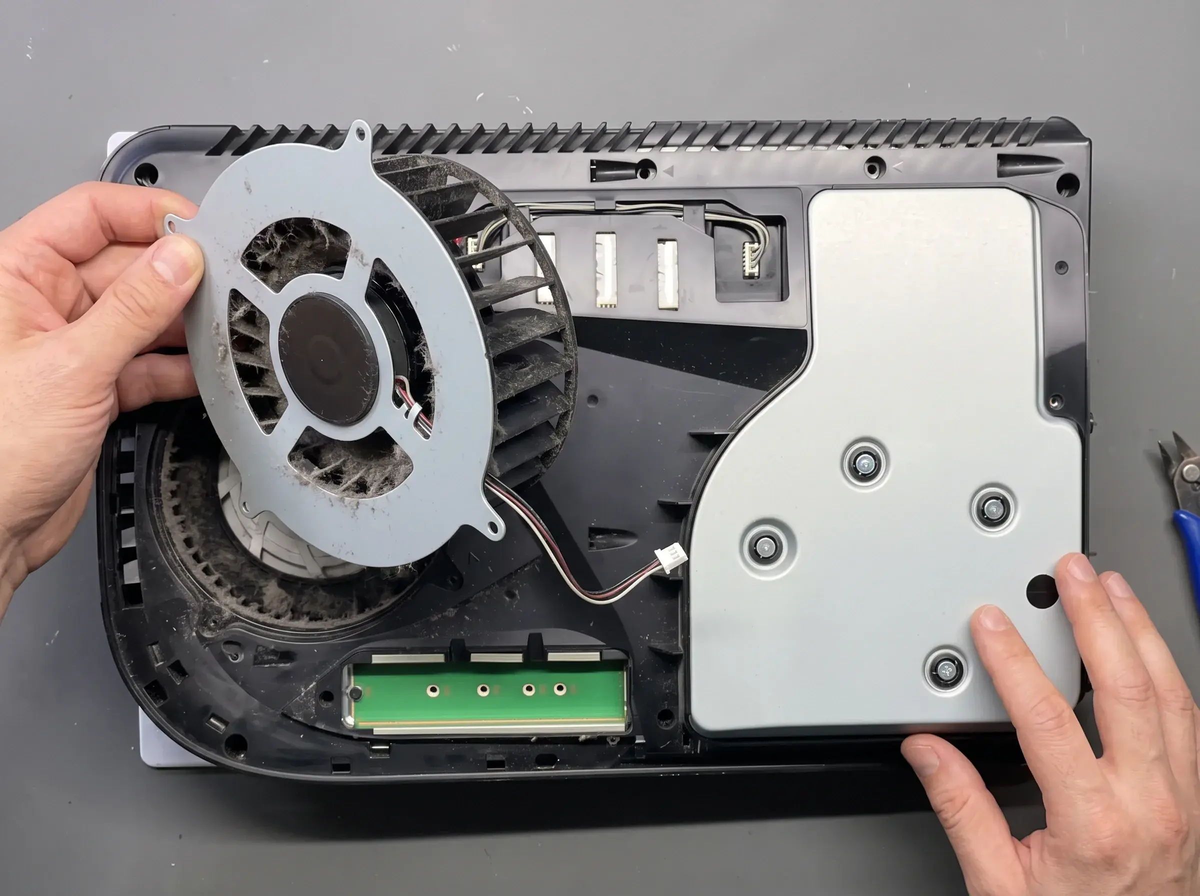 A hand lifts a dusty fan out of an opened PS5