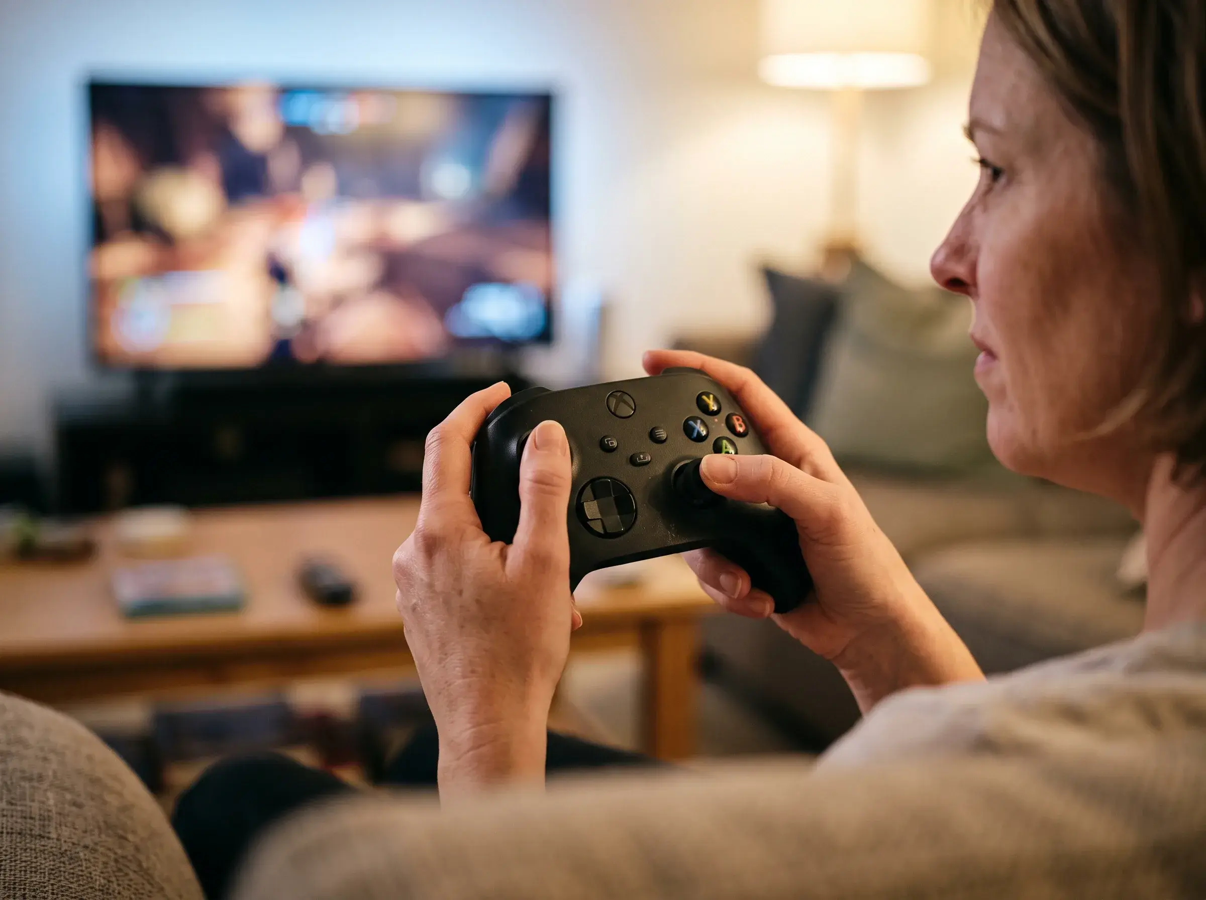 A player holds a black Xbox Series X|S controller in front of a TV at night
